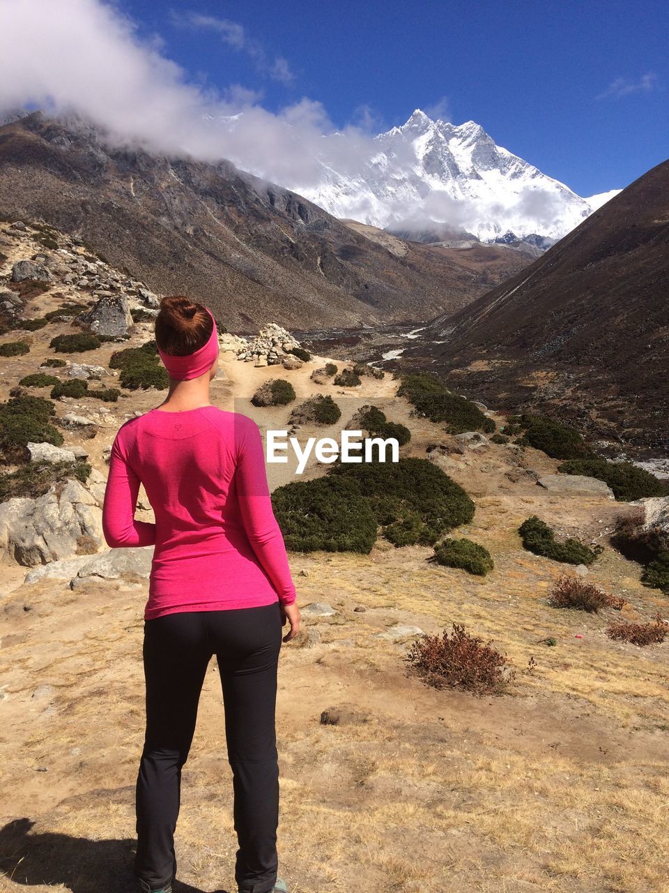 Rear view of young woman standing on field against sky during sunny day