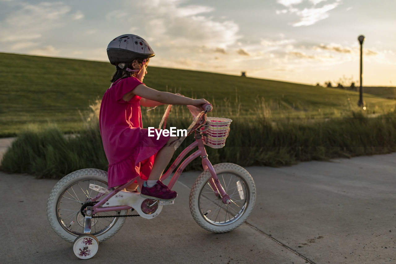 Side view of girl learning to ride bicycle on road against sky