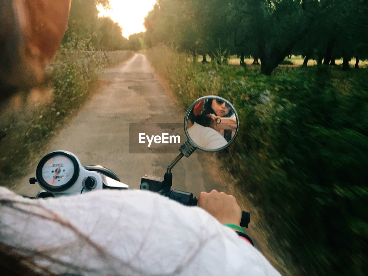 Friends reflecting on side-view mirror of motor scooter at road