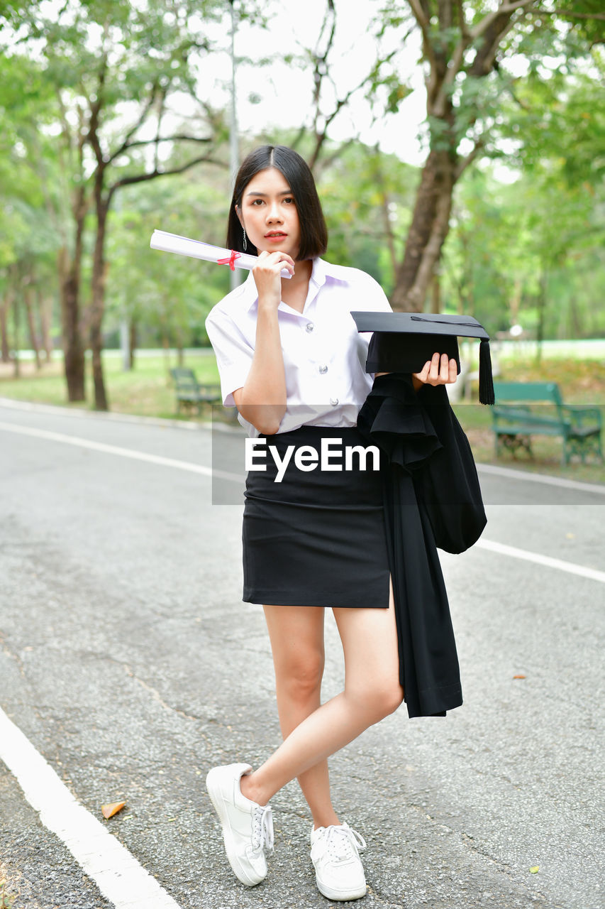 Student wearing graduation gown while standing on road at park