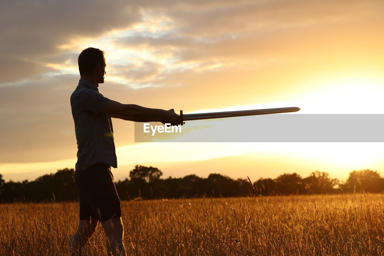 MAN STANDING ON FIELD AGAINST ORANGE SKY