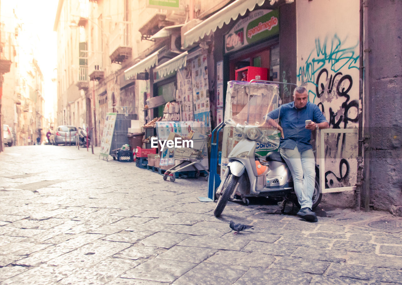 MAN SITTING ON FOOTPATH AMIDST STREET