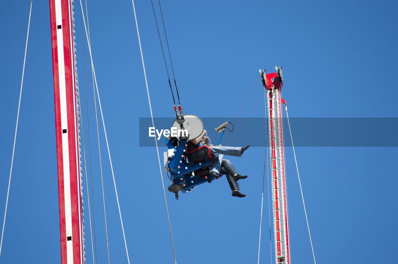 Low angle view of friends sitting on amusement park ride against clear blue sky