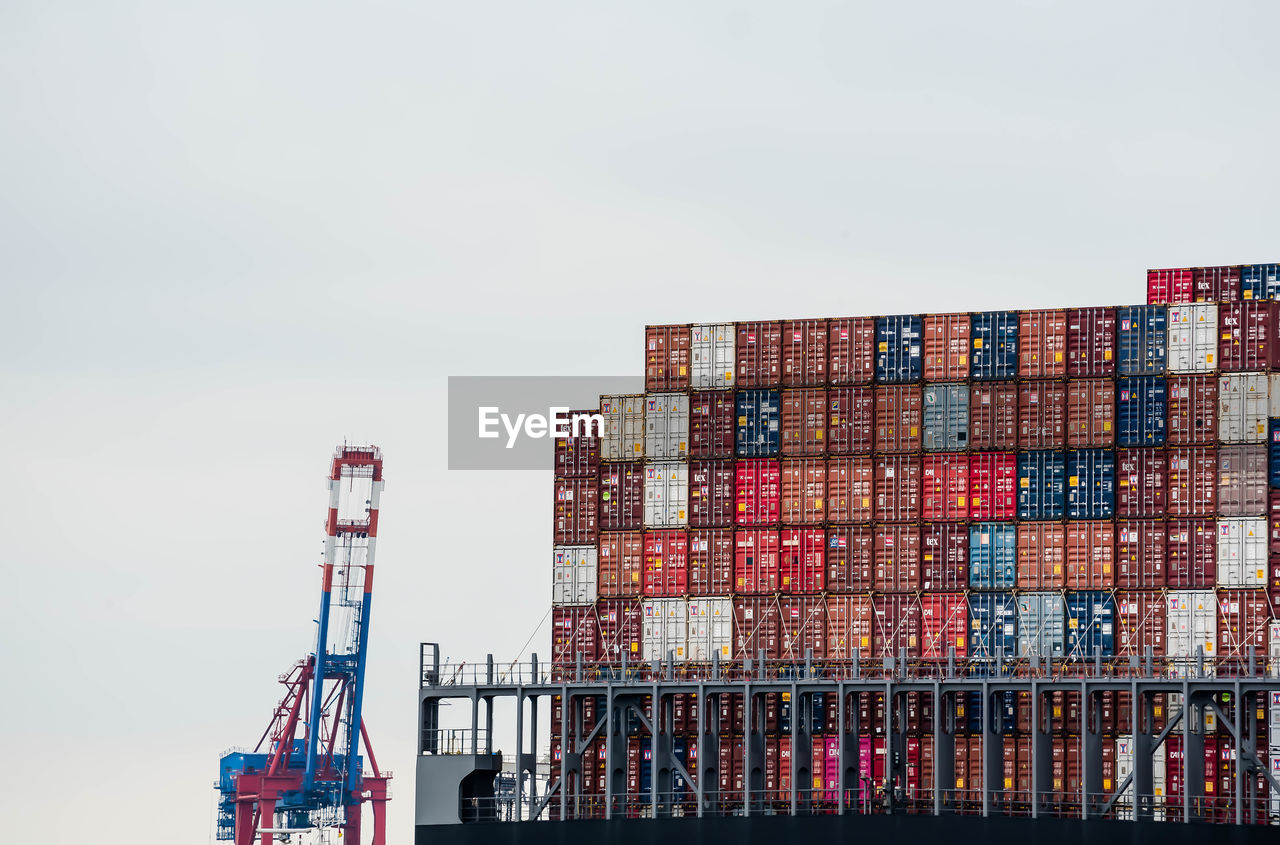 Low angle view of cranes and cargo containers against sky