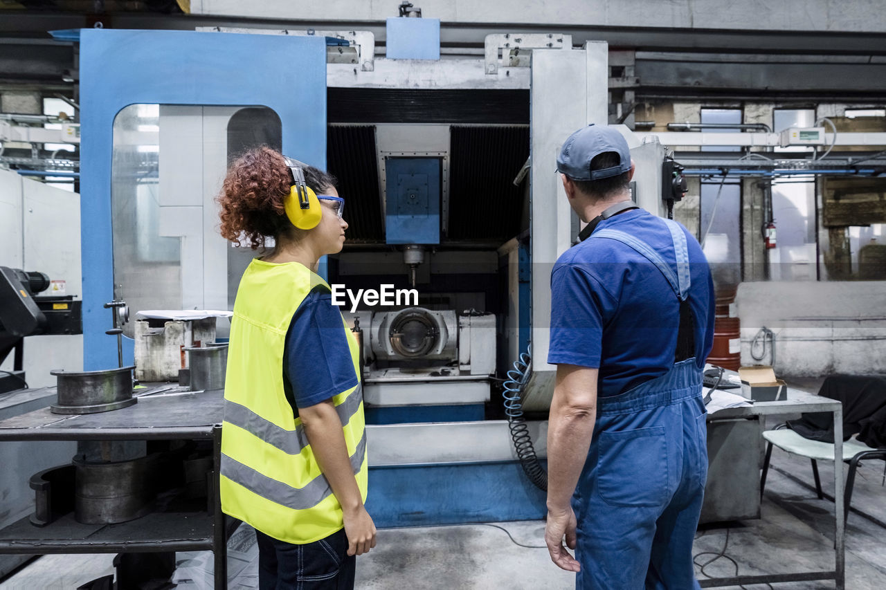 Maintenance engineer examining coworker working on machinery in modern factory