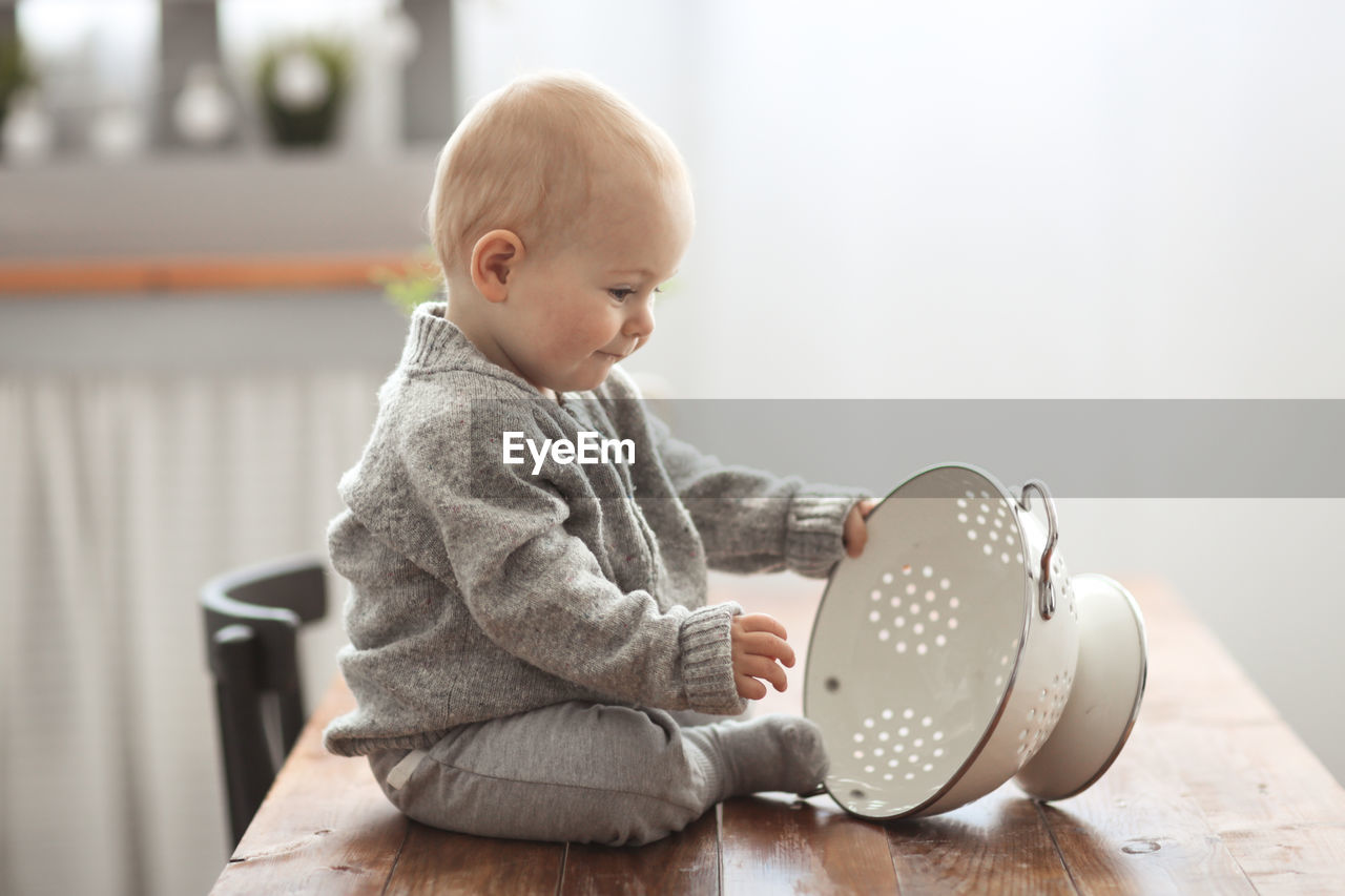 Baby of 10 months plays on the table in the kitchen with kitchen utensils, the concept 