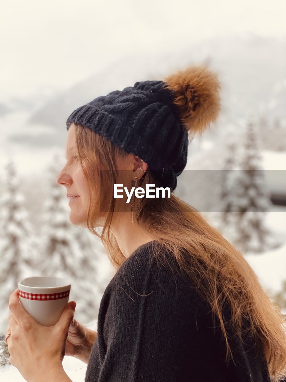 Woman with coffee cup against snow covered land