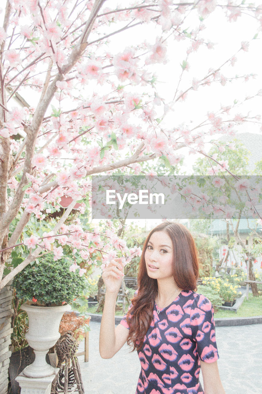 PORTRAIT OF BEAUTIFUL WOMAN STANDING BY PINK FLOWERS