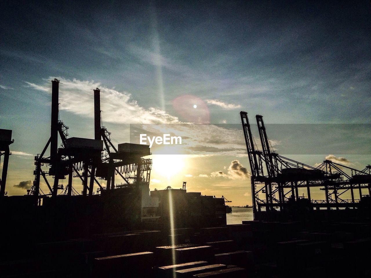 Cranes and containers at harbor during sunset