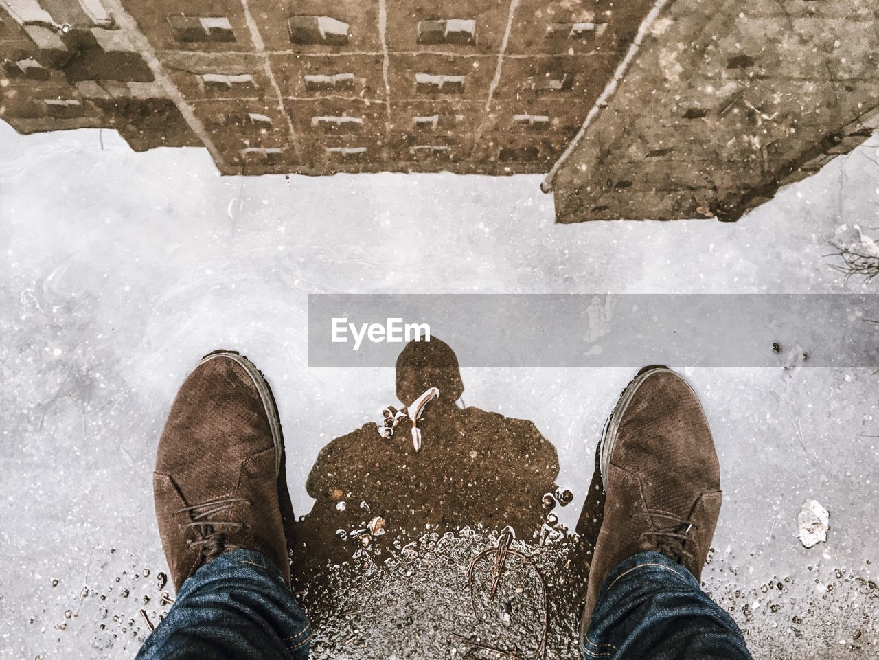 Low section of man standing by puddle with building reflection