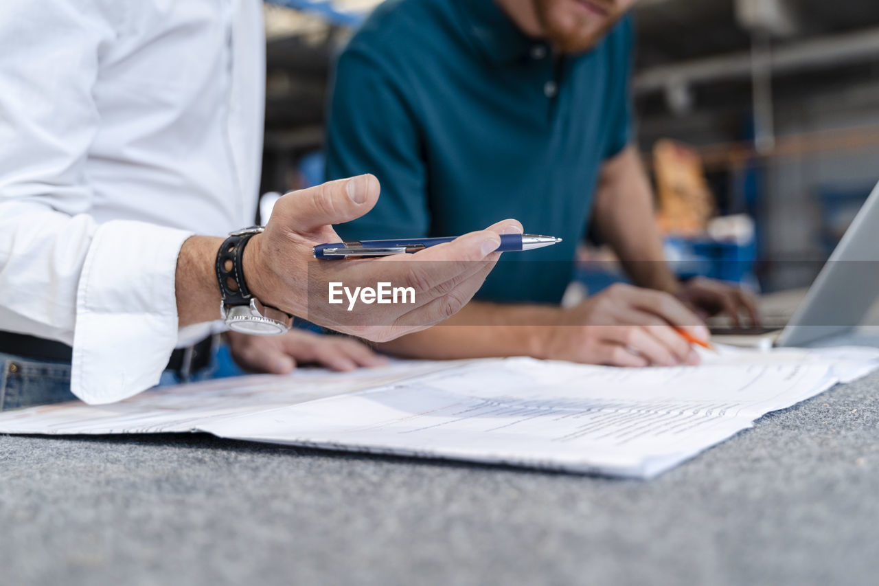 Hand of man holding pen while talking over documents with coworker