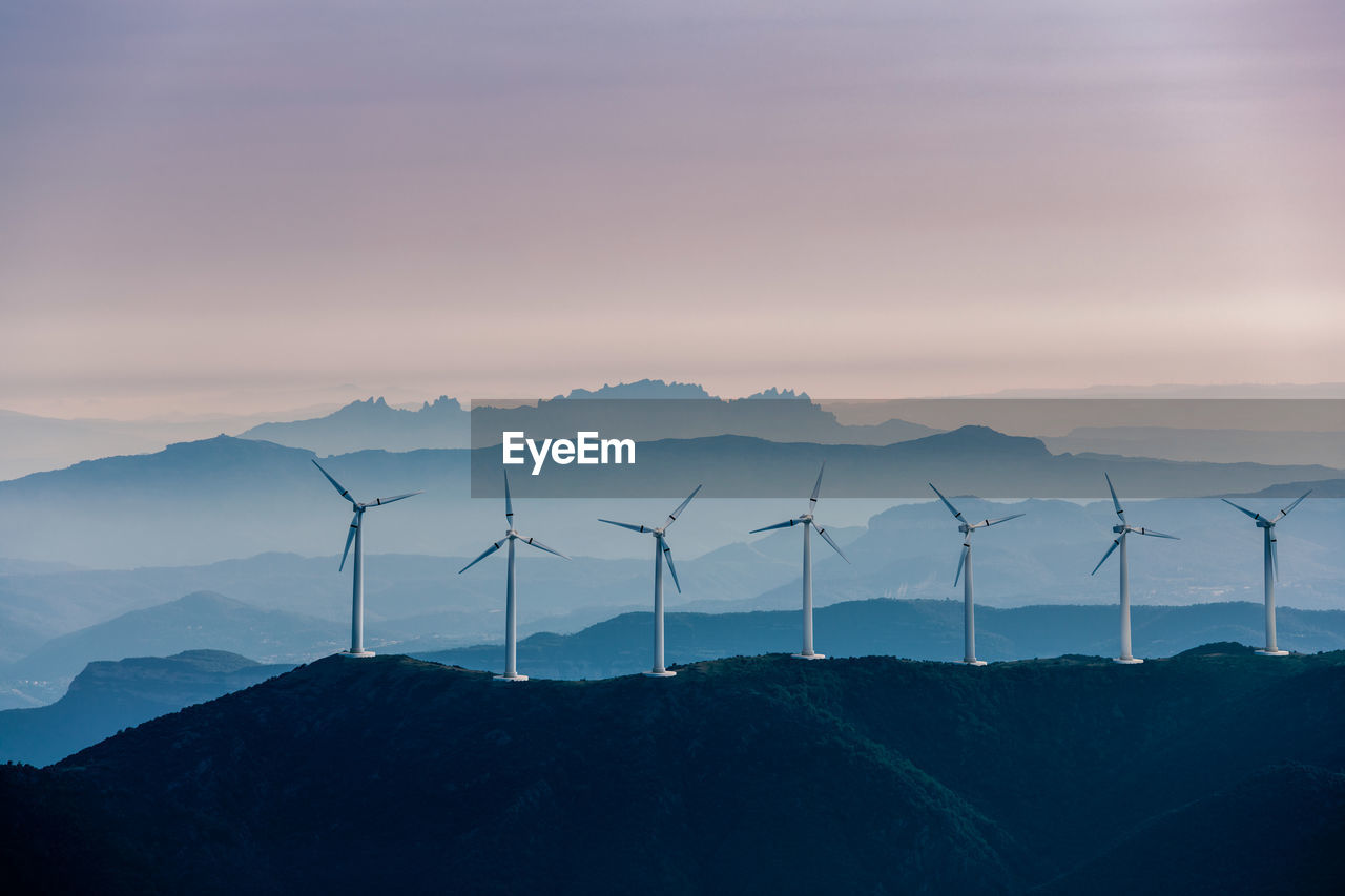 Wind turbines on mountain against sky during sunset