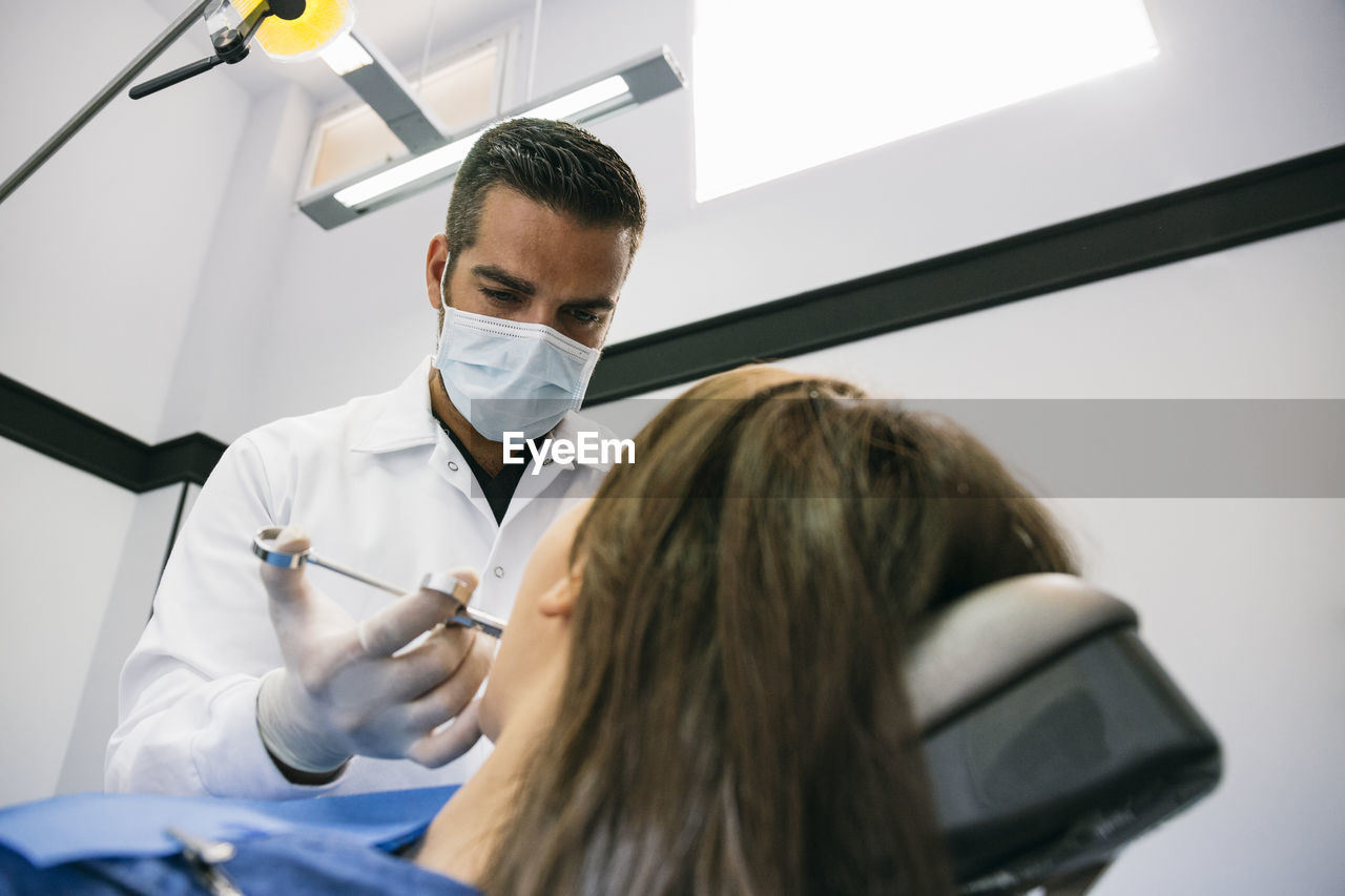 Male dentist anesthetizing female patient before dental treatment at clinic