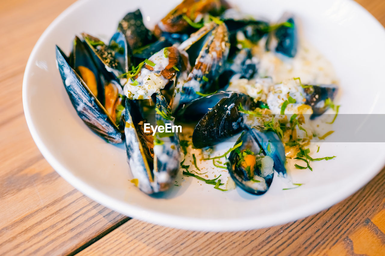Close up of freshly cooked mussles in a plate with ingredients.