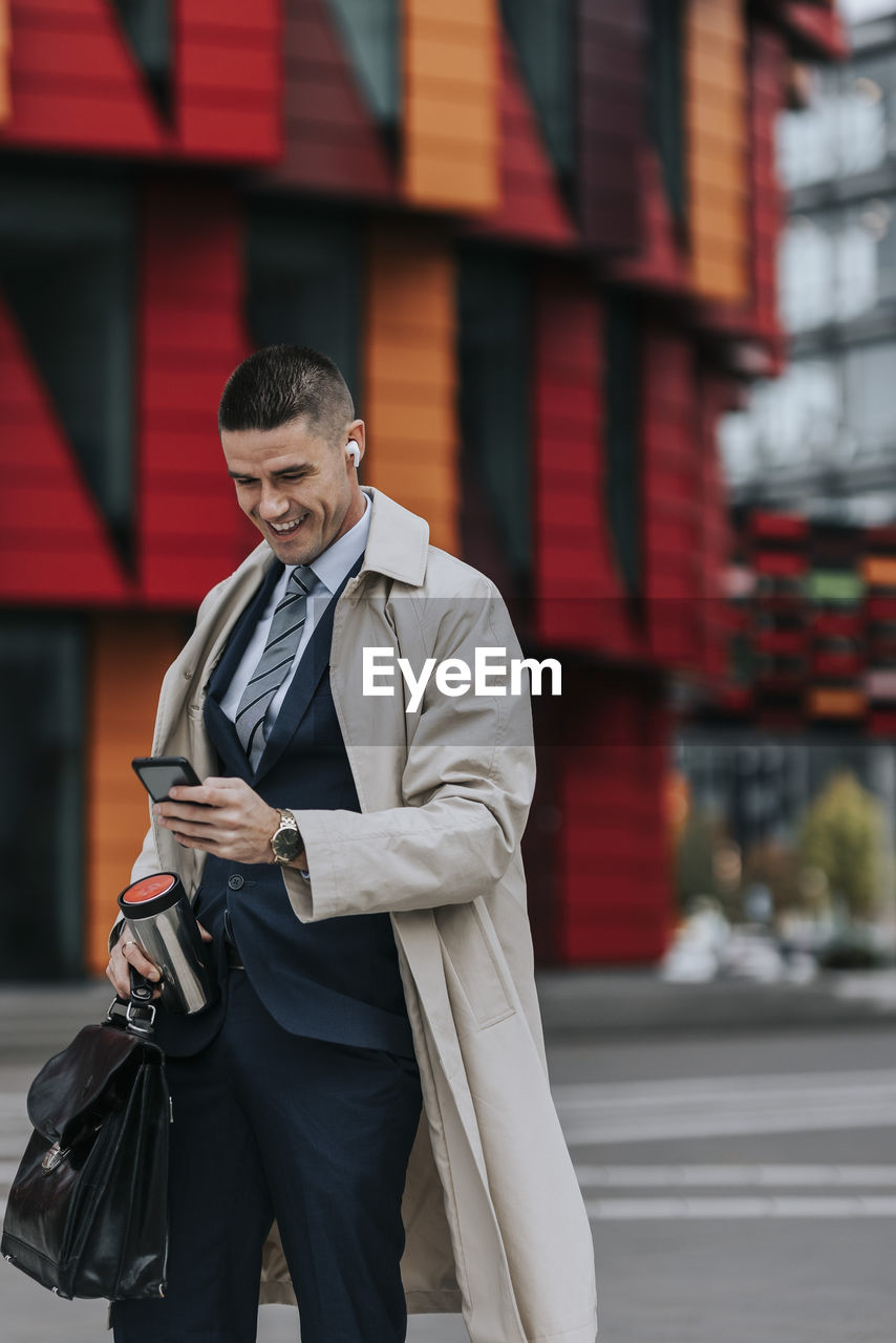 Happy businessman using smart phone while standing at street