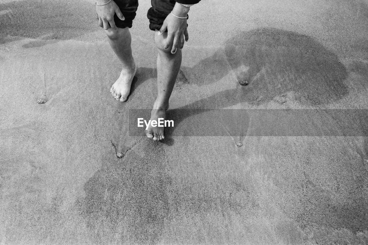 Low section view of man rolling up pants on beach