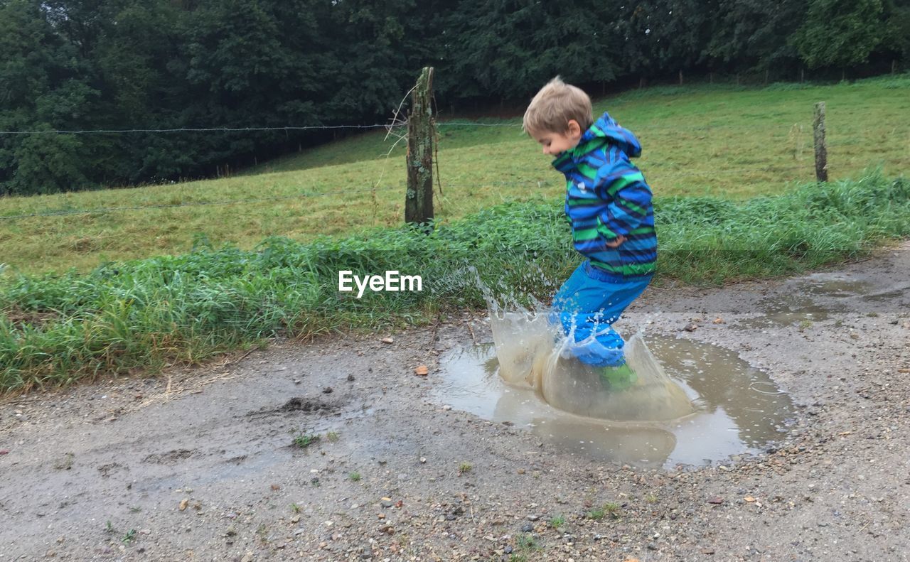Playful boy jumping in puddle