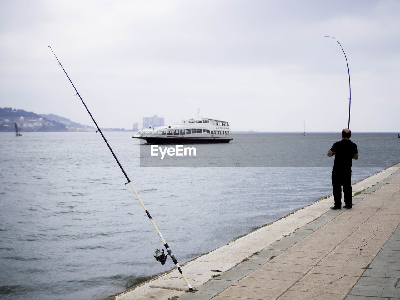 REAR VIEW OF MAN FISHING AT SEA AGAINST SKY