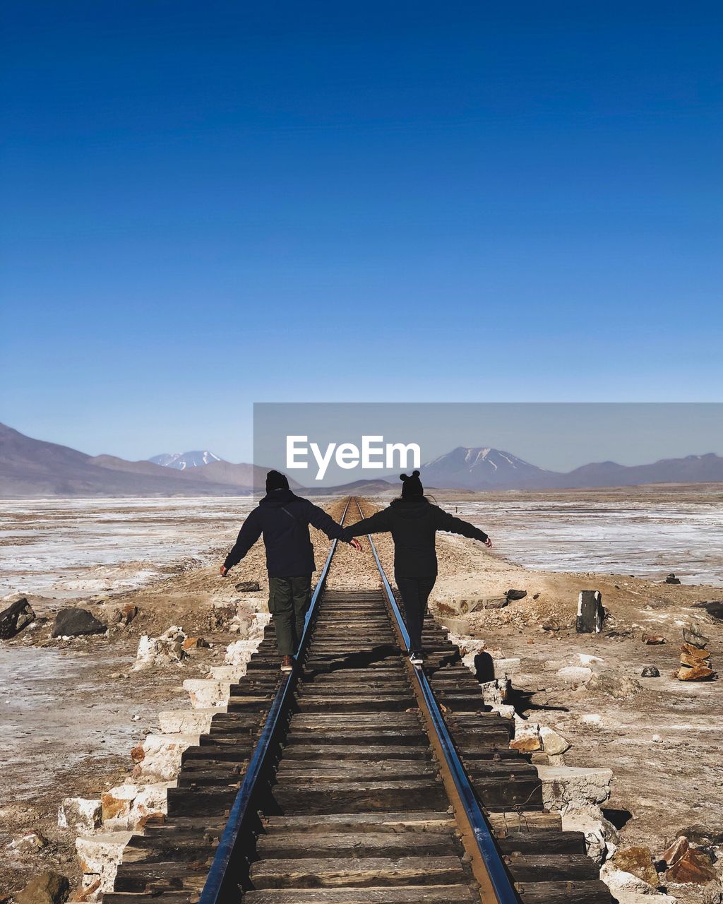 Rear view of people walking on railroad track against clear blue sky