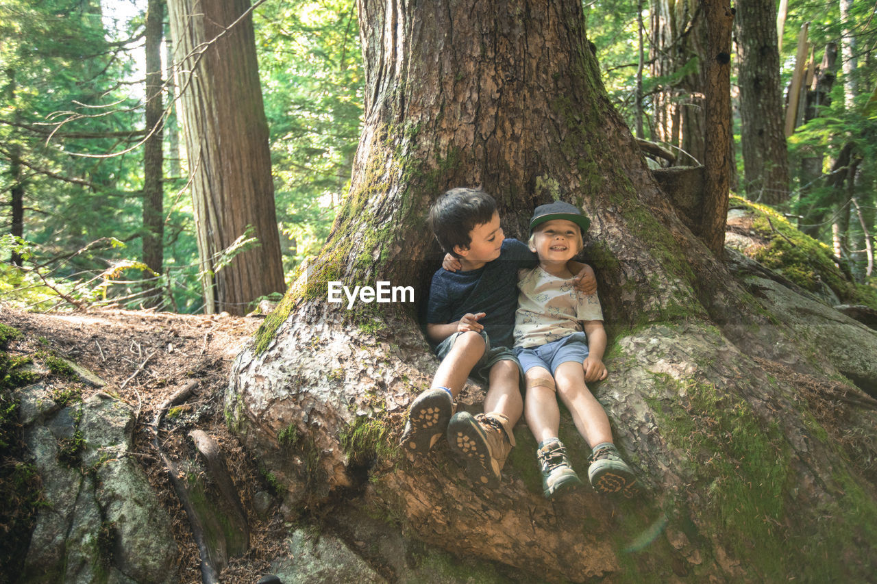 Two young boy friends embrace happily under large tree