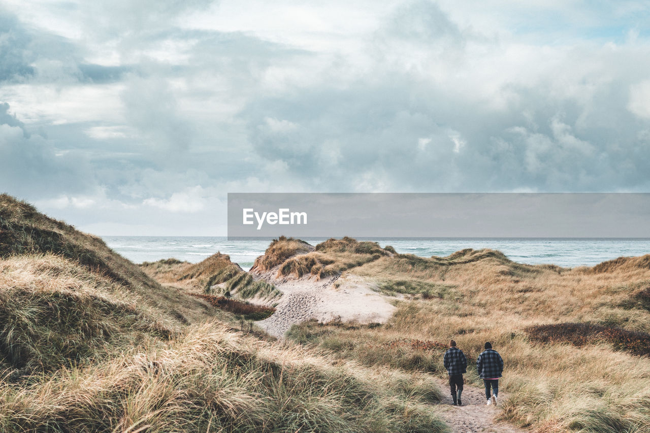 Rear view of people walking on land against sea and sky