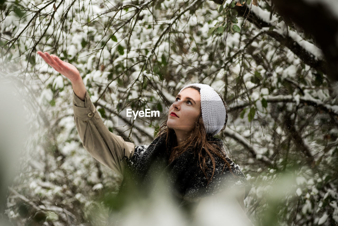 PORTRAIT OF YOUNG WOMAN IN SNOW COVERED TREE