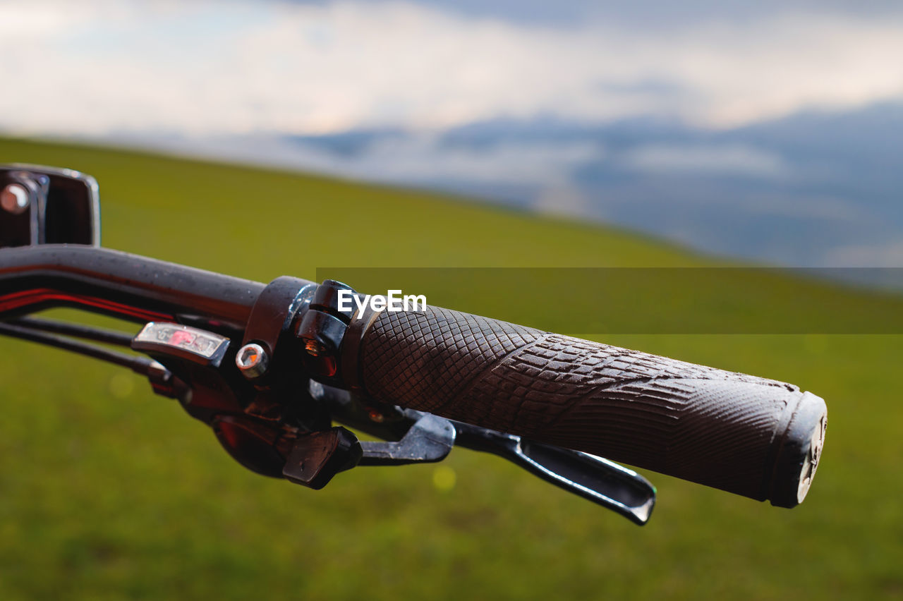 Close-up of a mountain bike handle against the background of green meadows of mountains and clouds