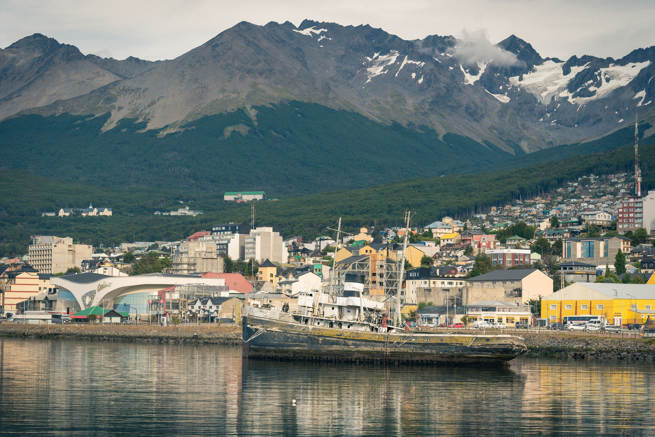 SCENIC VIEW OF RIVER BY TOWNSCAPE AGAINST MOUNTAINS