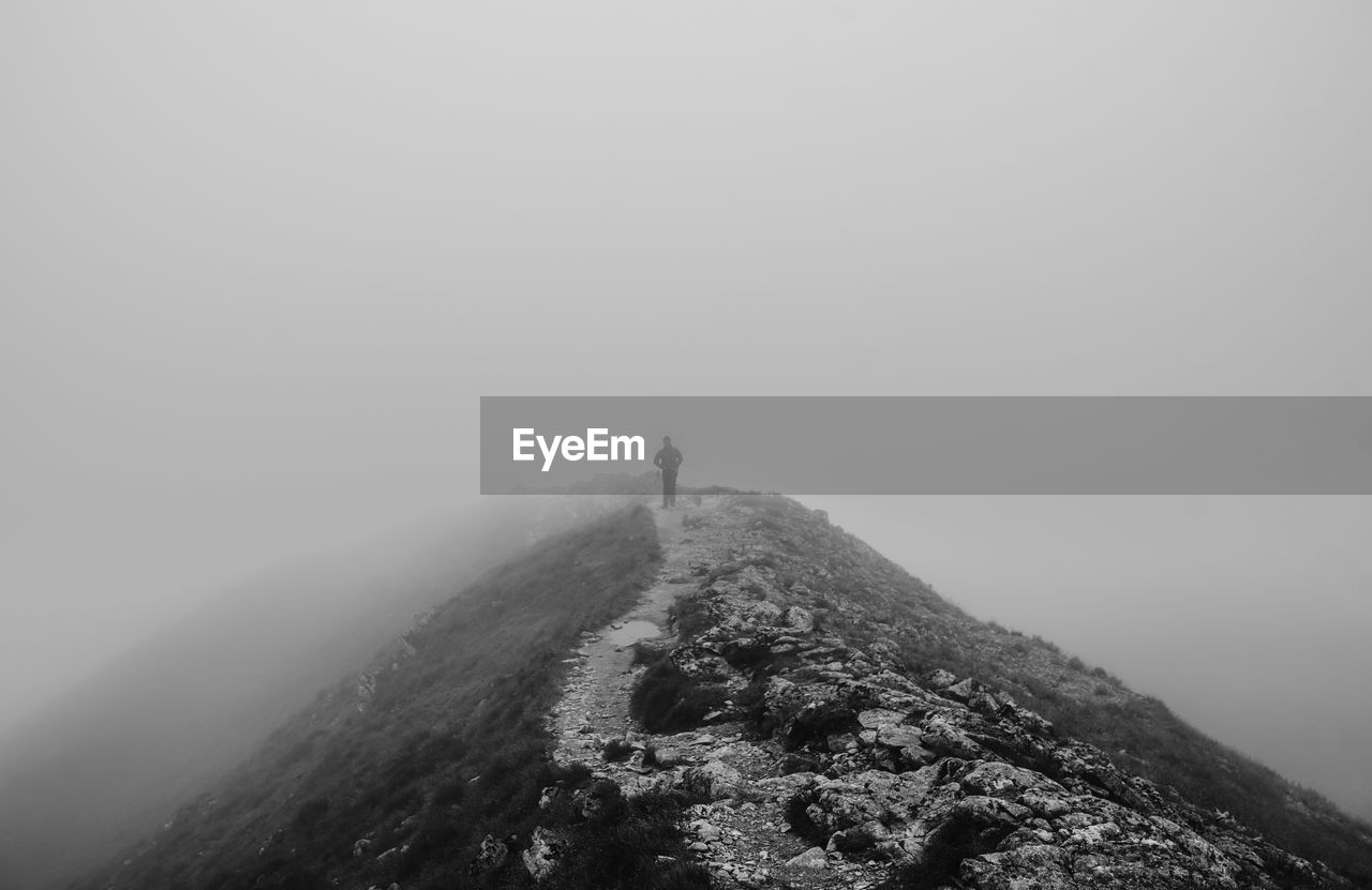 Distant view of person walking on hill during foggy weather