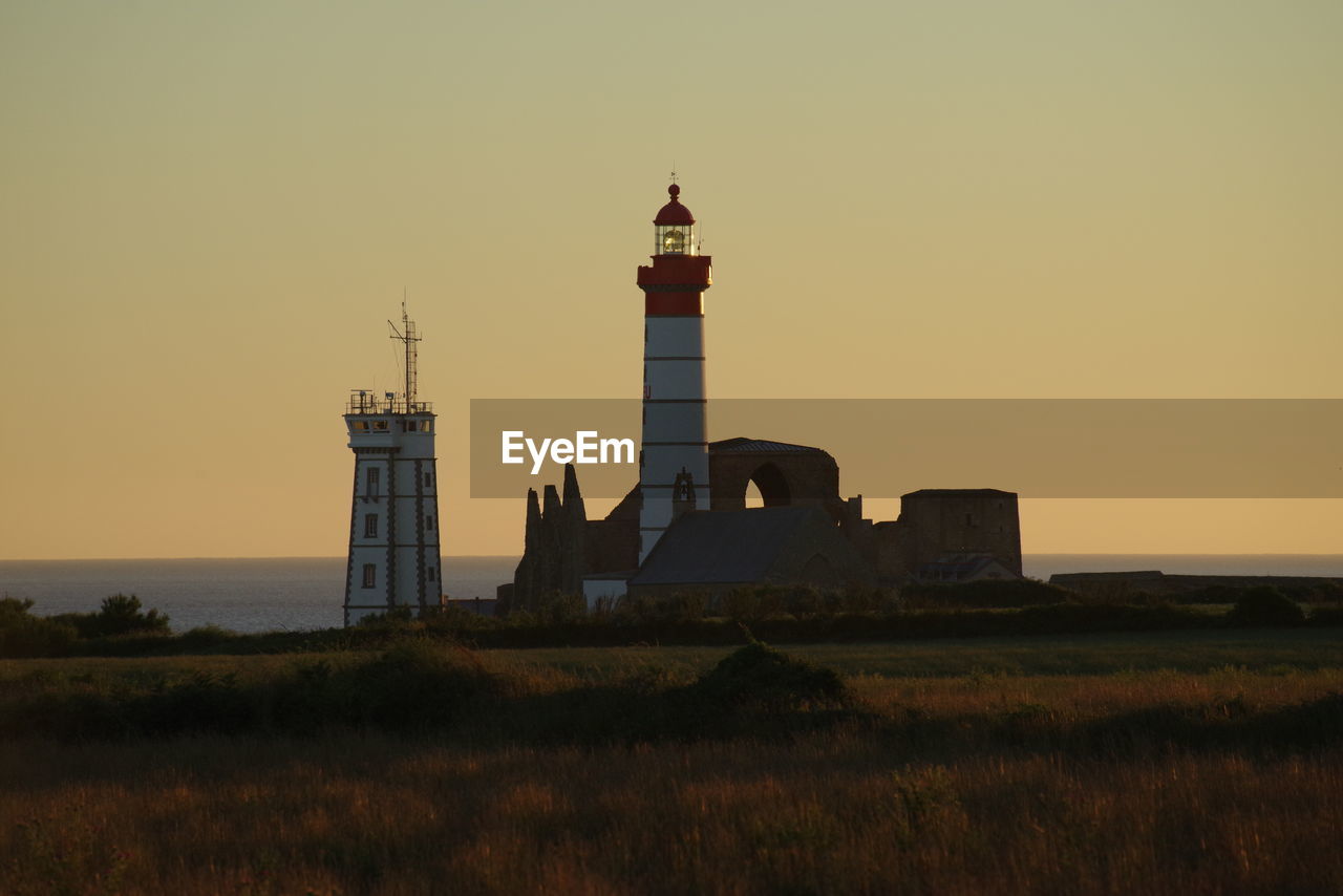 LIGHTHOUSE ON FIELD AGAINST SKY AT SUNSET