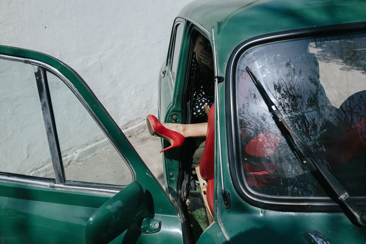 Women sitting in green vintage car against wall