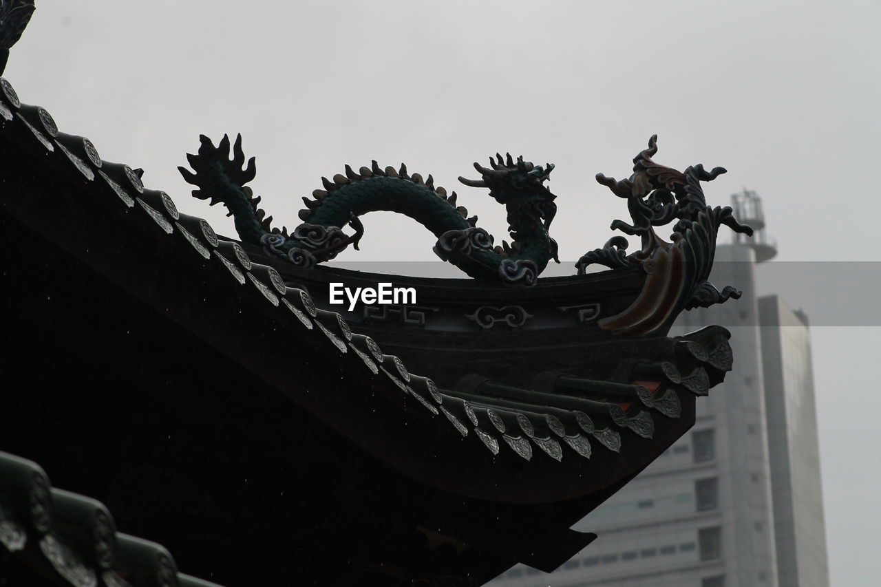 Low angle view of dragon sculpture on roof against clear sky