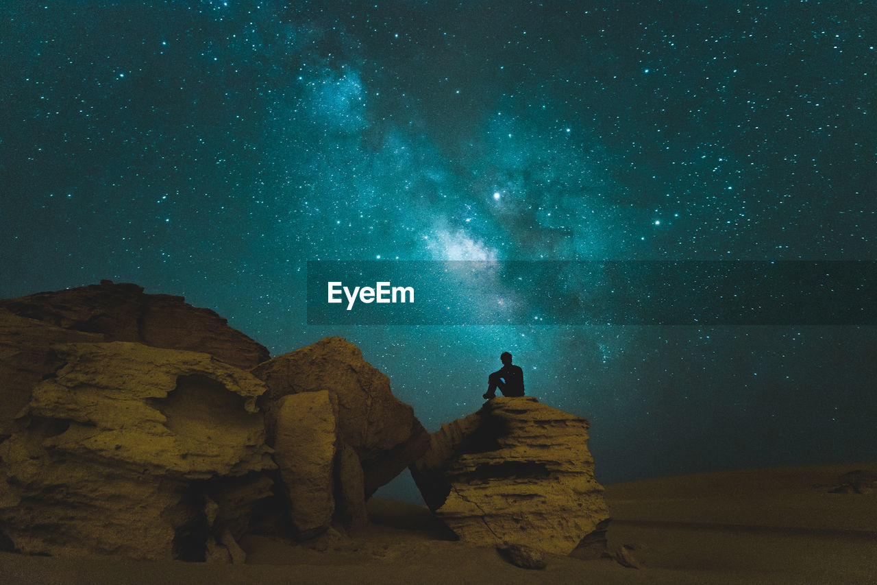 Man sitting on rock against star field