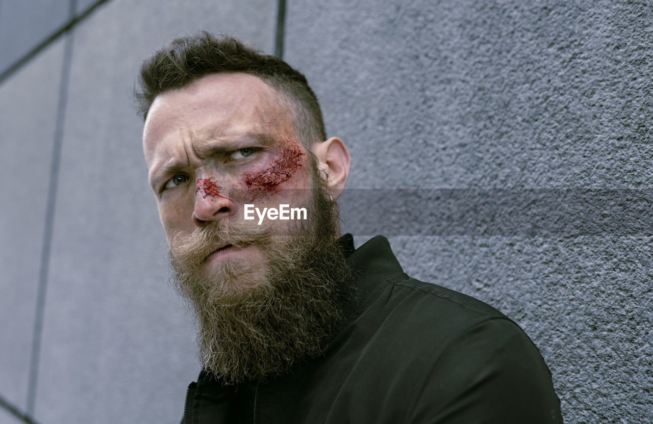 Side view hipster man with beard and cinema makeup posing on the street