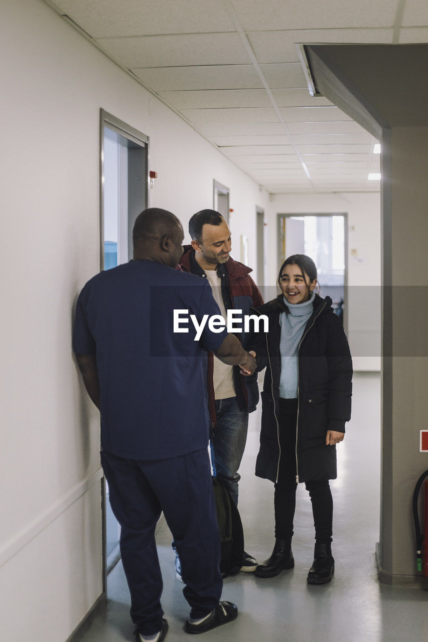 Smiling girl doing handshake with doctor standing at hospital corridor