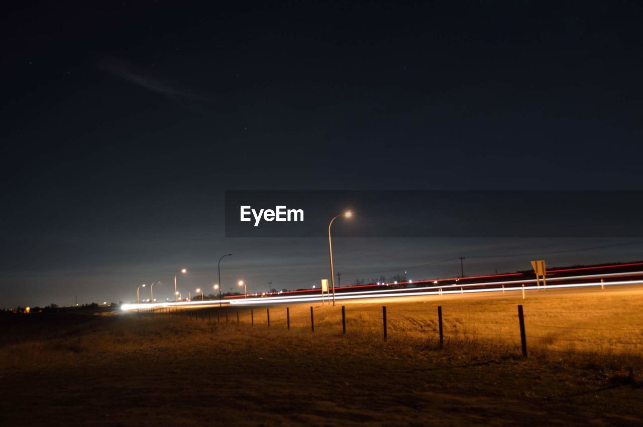 Light trails by field against sky at night