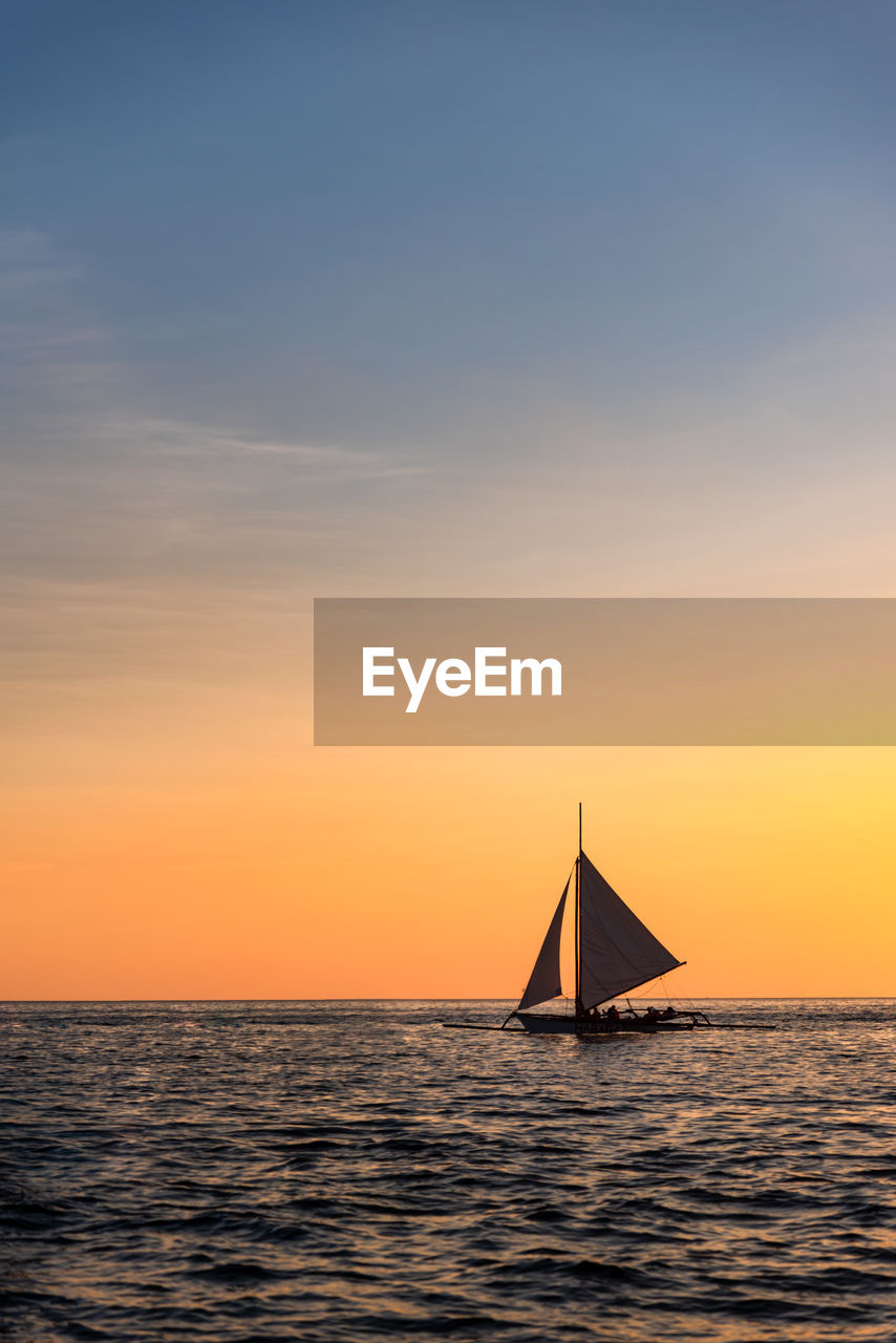 Sailboat sailing on sea against sky during sunset