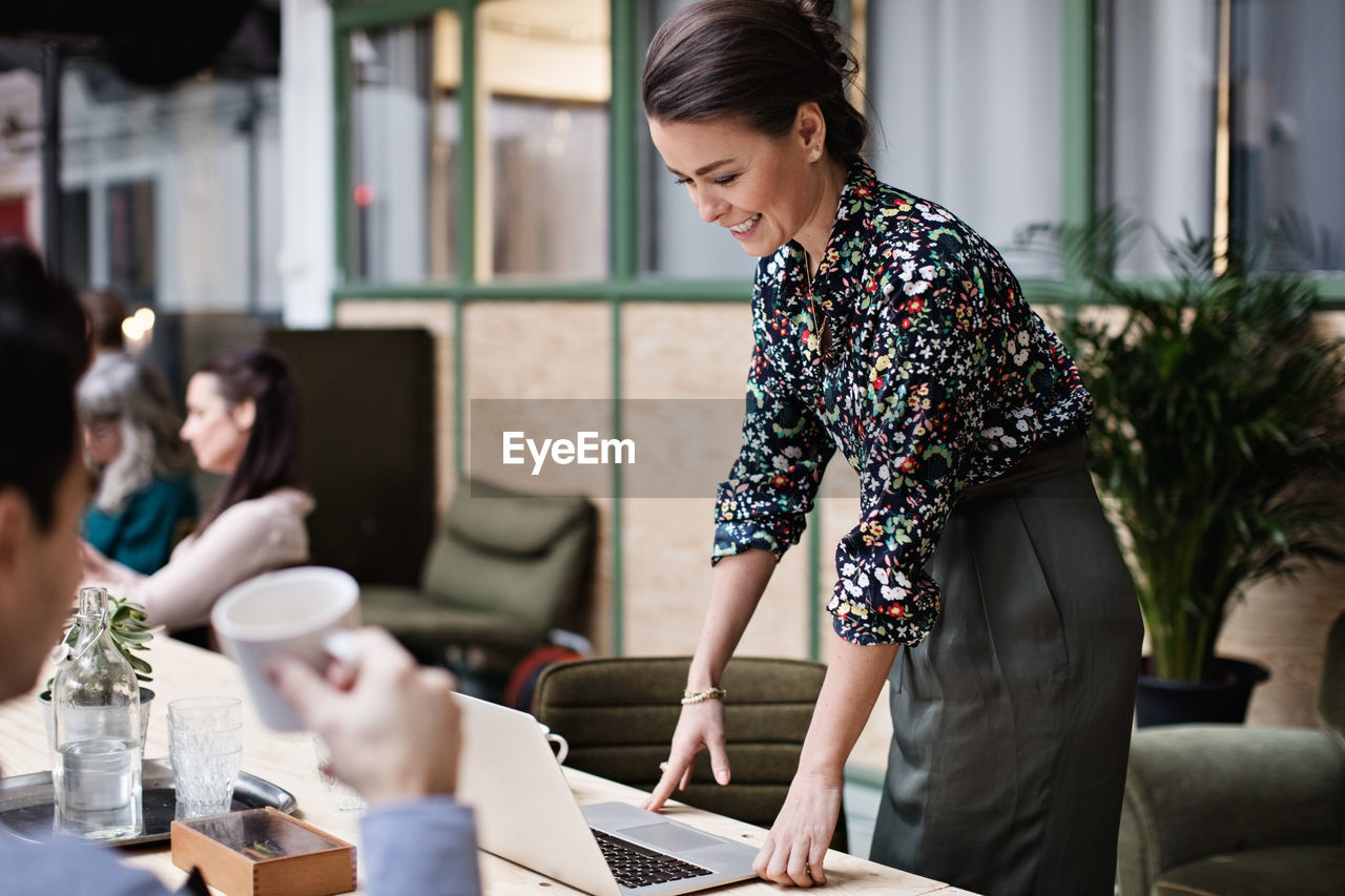 Smiling businesswoman using laptop while looking at coworker in office