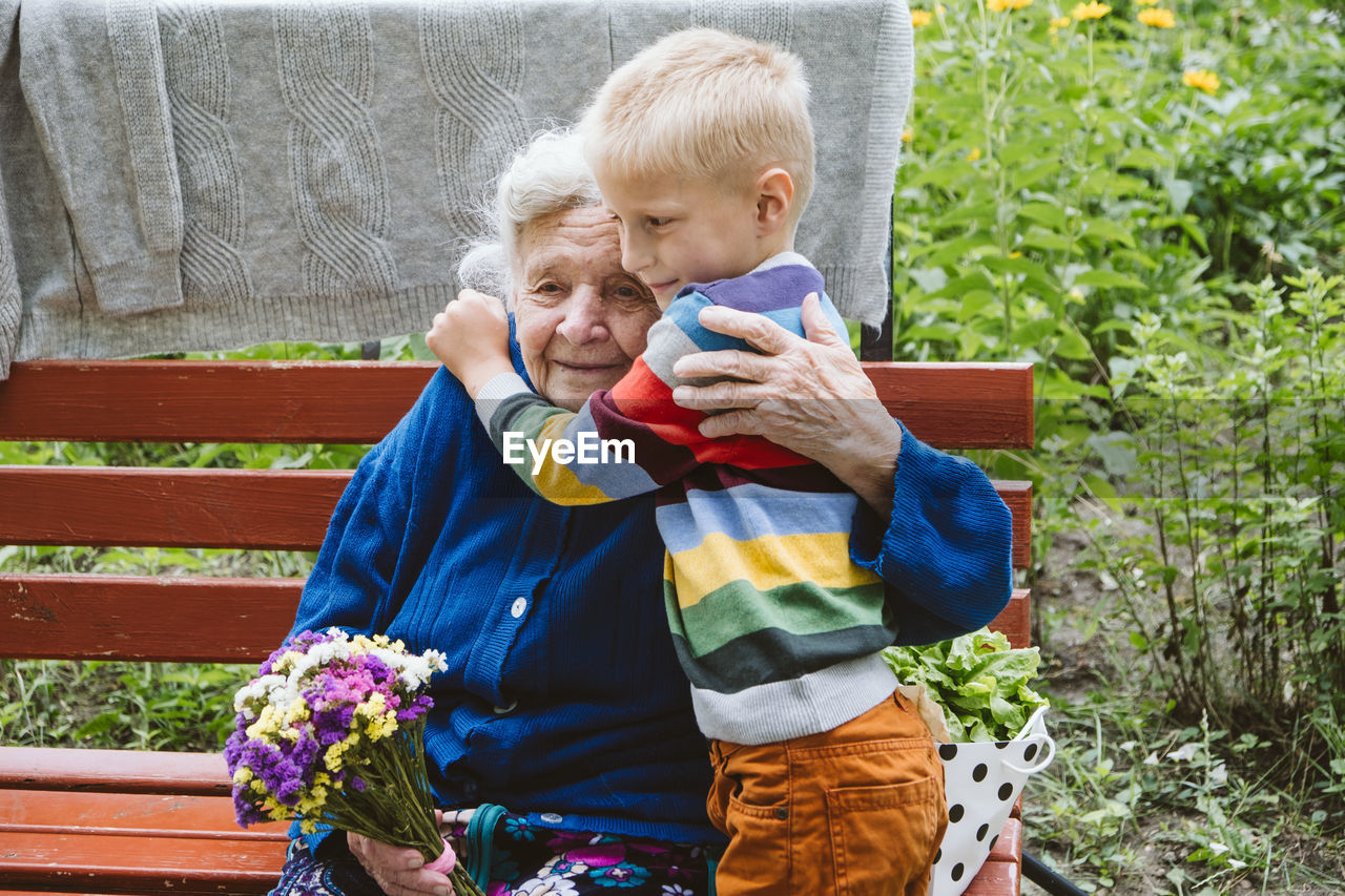 Grandmother and grandson embracing while sitting at park