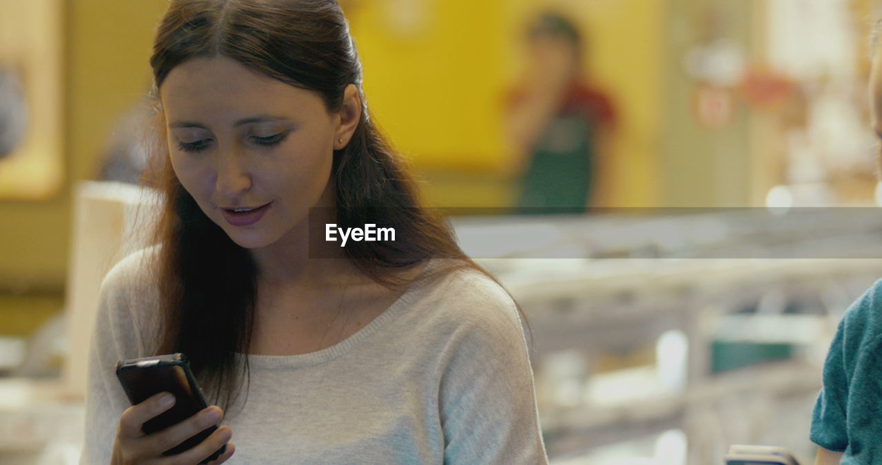 PORTRAIT OF YOUNG WOMAN USING MOBILE PHONE IN CAMERA