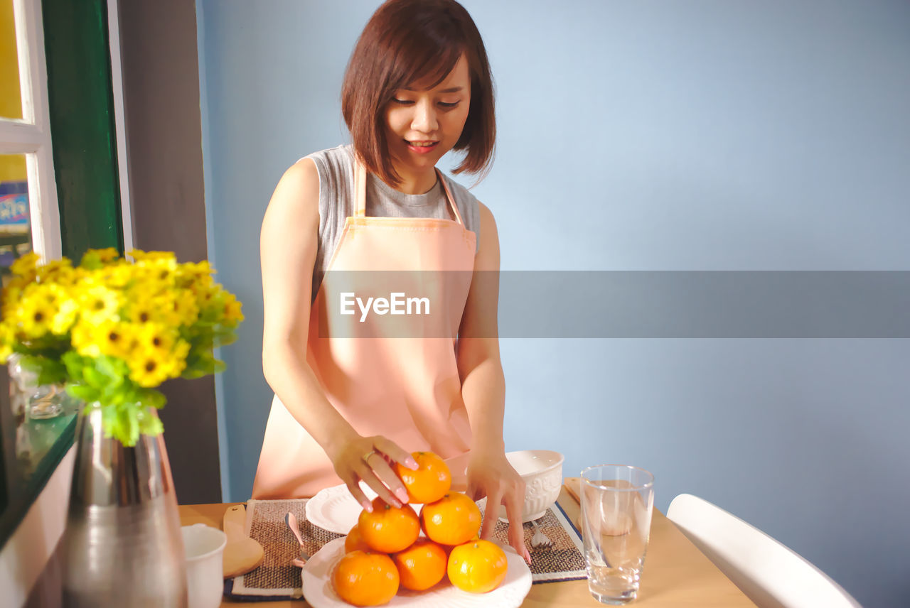 Woman stacking oranges on table at home