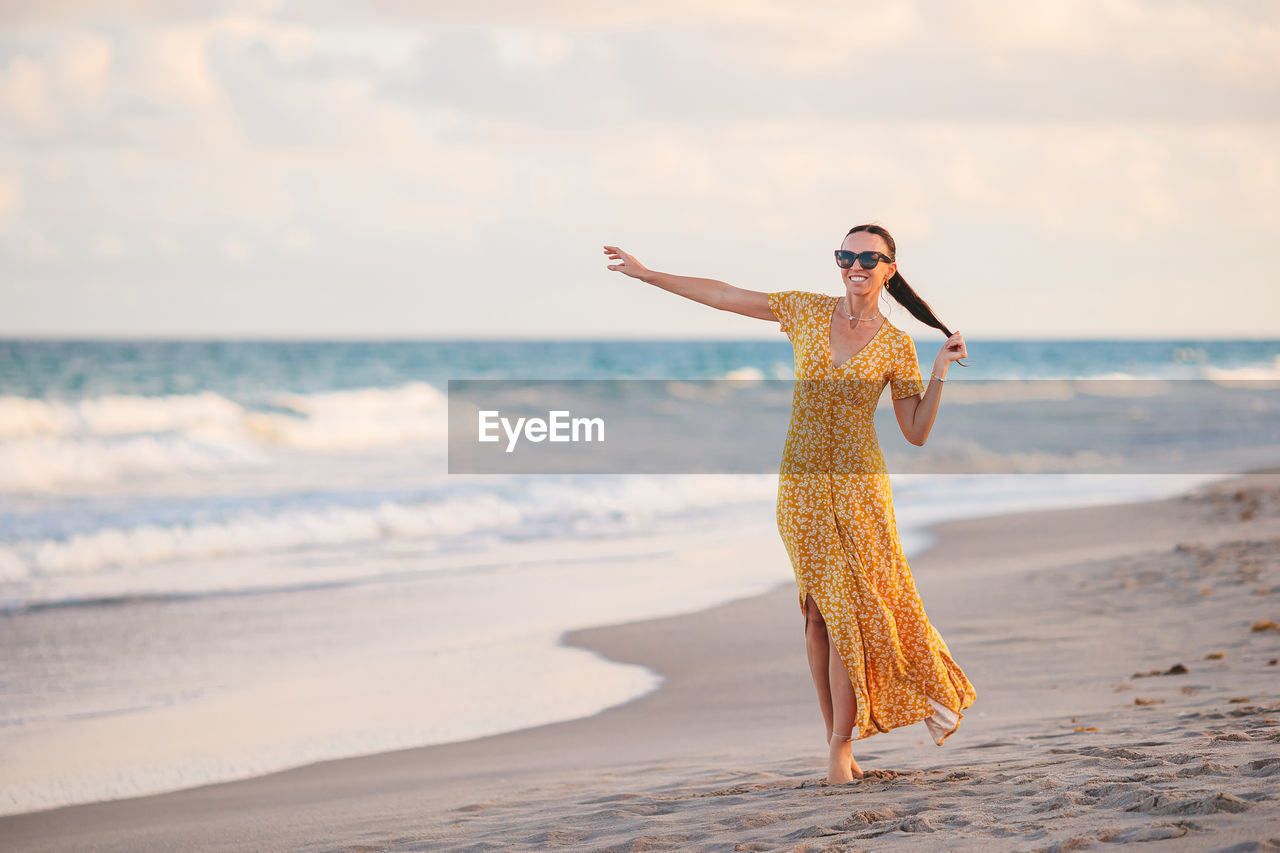 young woman standing at beach against sky