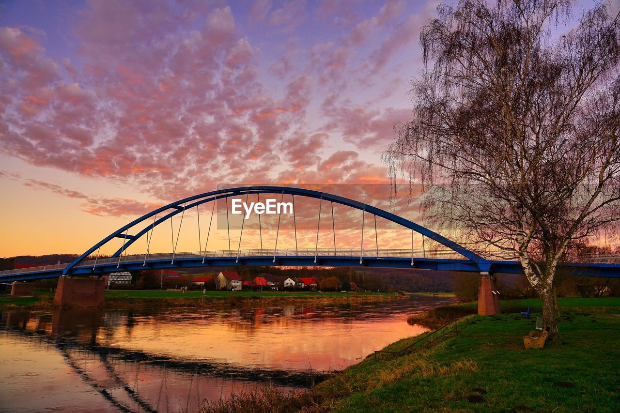 Arch bridge over river against sky during sunset