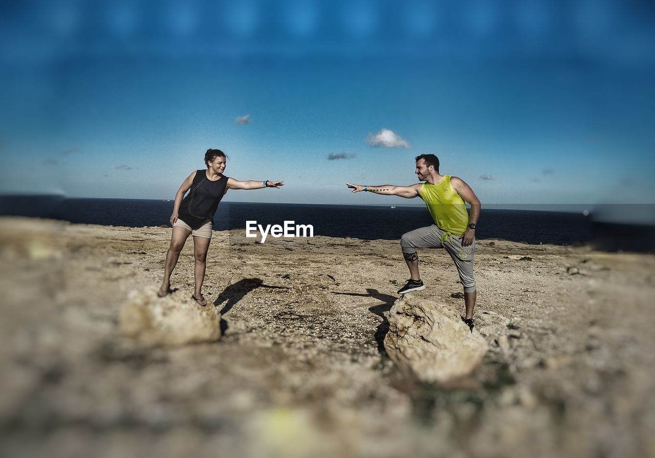 Friends enjoying while standing on rocks against sea at beach