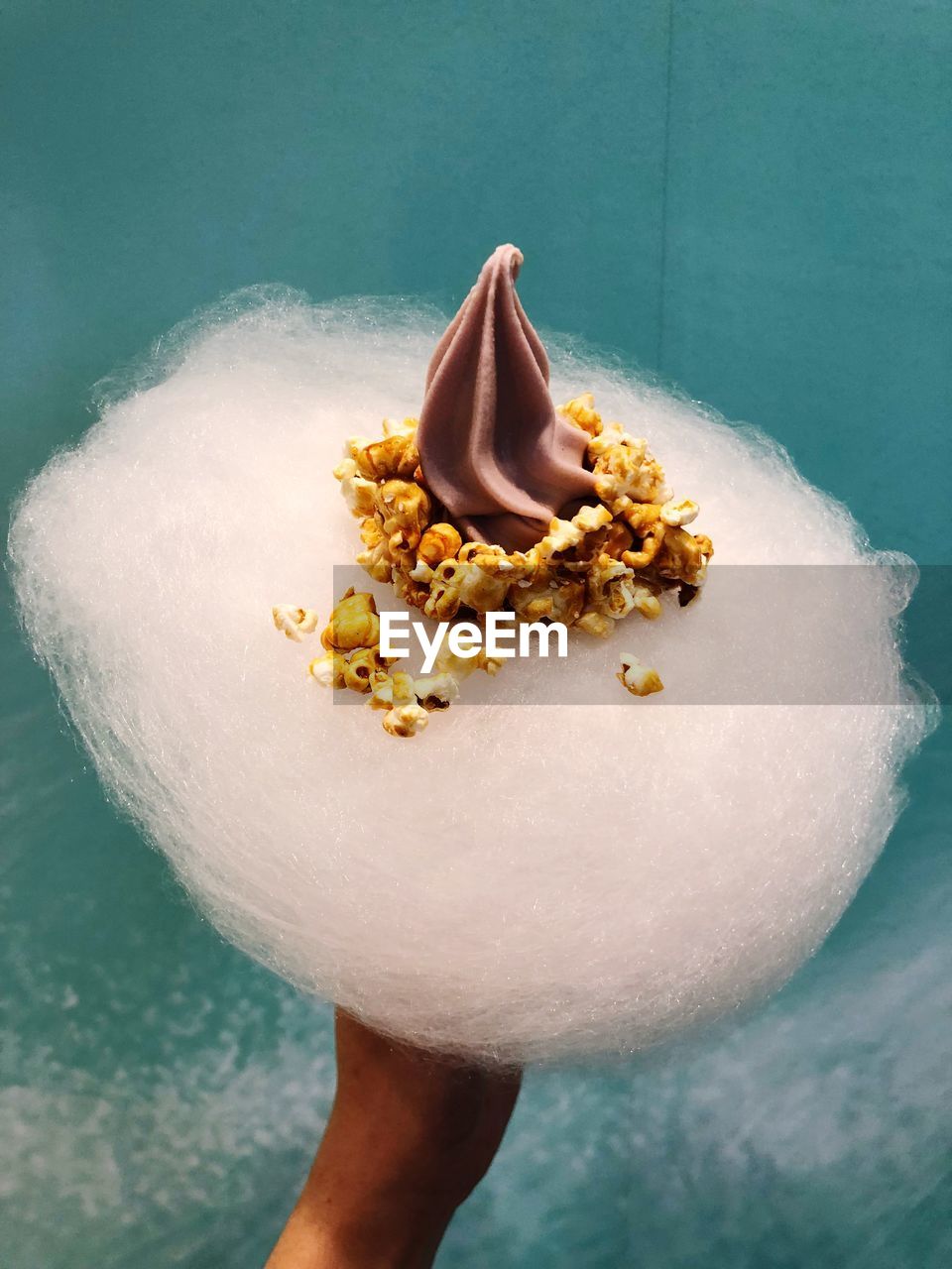 Cropped image of hand holding cotton candy with popcorn and whipped cream