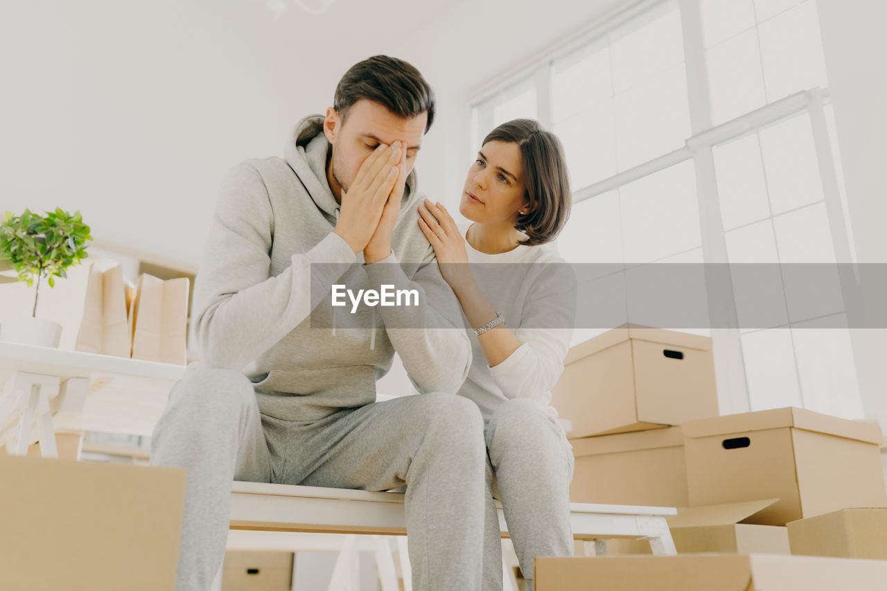 Woman consoling tired man sitting by boxes at home
