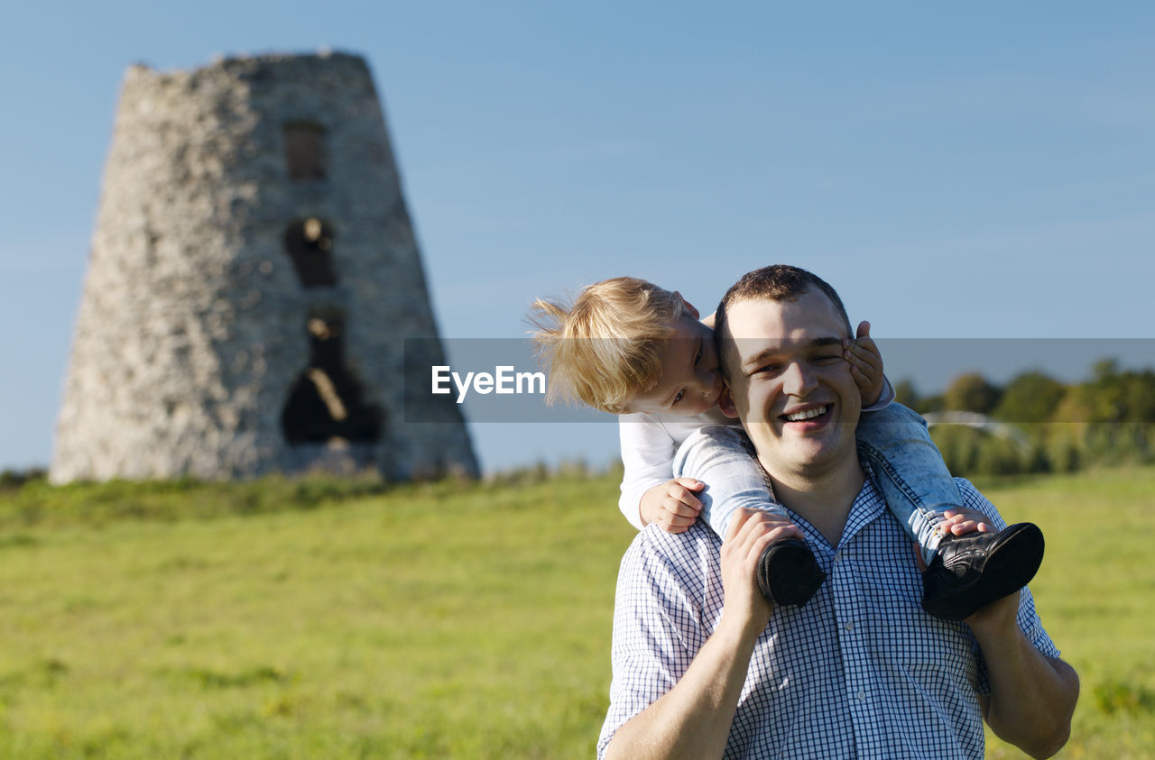 Happy father giving piggyback to son against old built structure on field