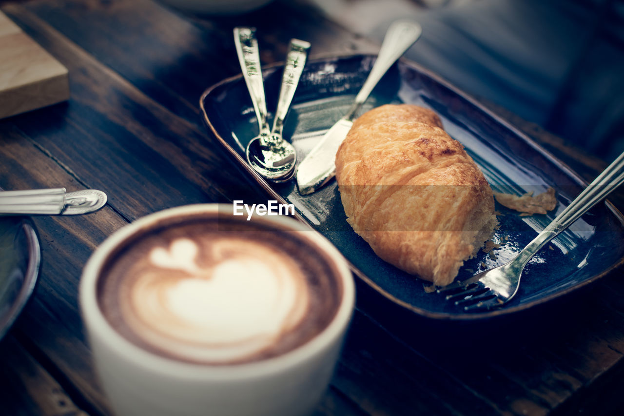 Croissant on wooden table with a cup of coffee, vintage color tone.