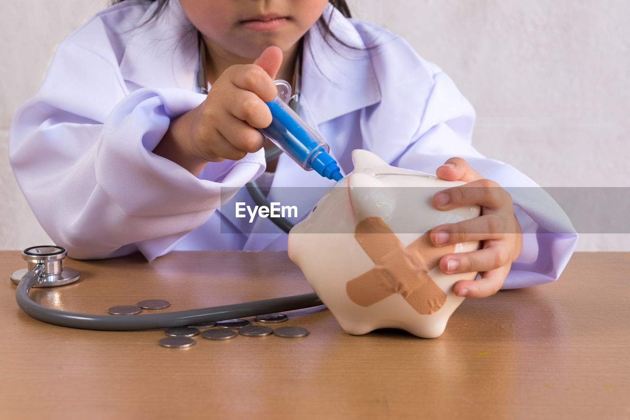 Midsection of doctor holding injection by piggy bank on table