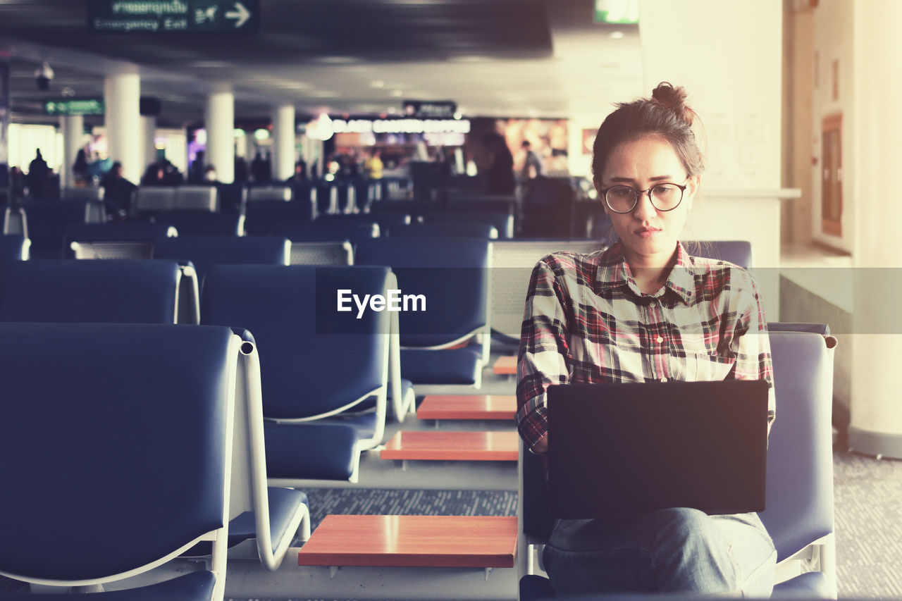 Woman using laptop while sitting at airport departure area